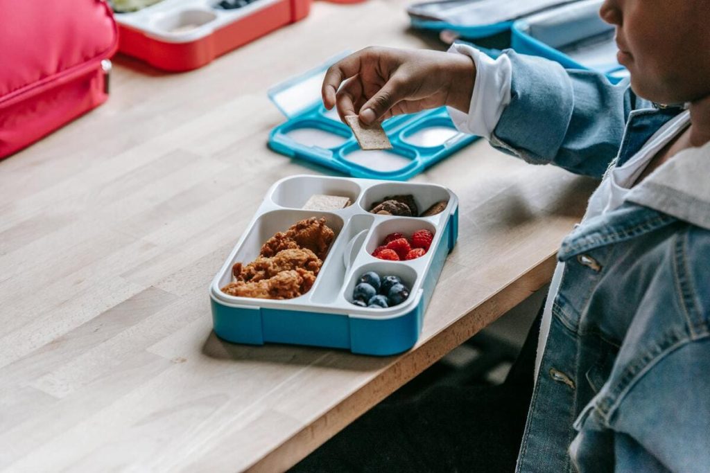 A black boy is putting some crackers in his lunchbox