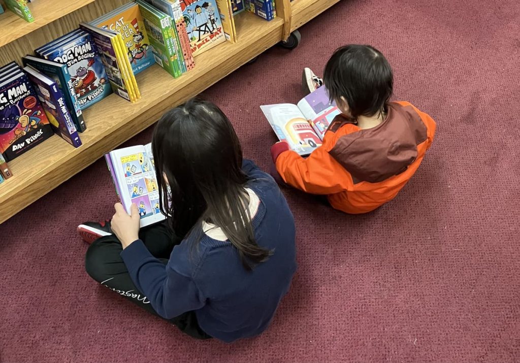 Two children are reading books sitting on the floor of a bookstore.
