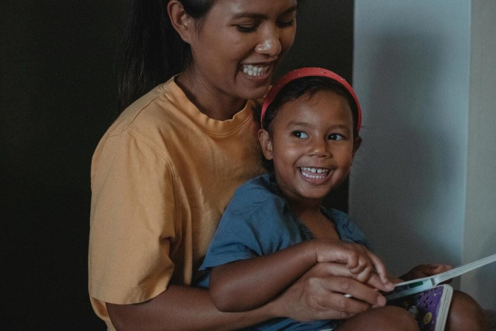 A mother and a child smiling while reading a book together